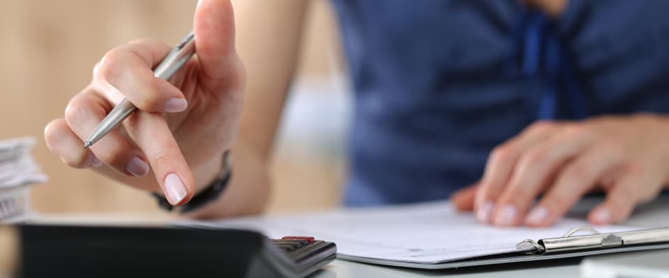 Hands signing insurance paperwork beside a calculator